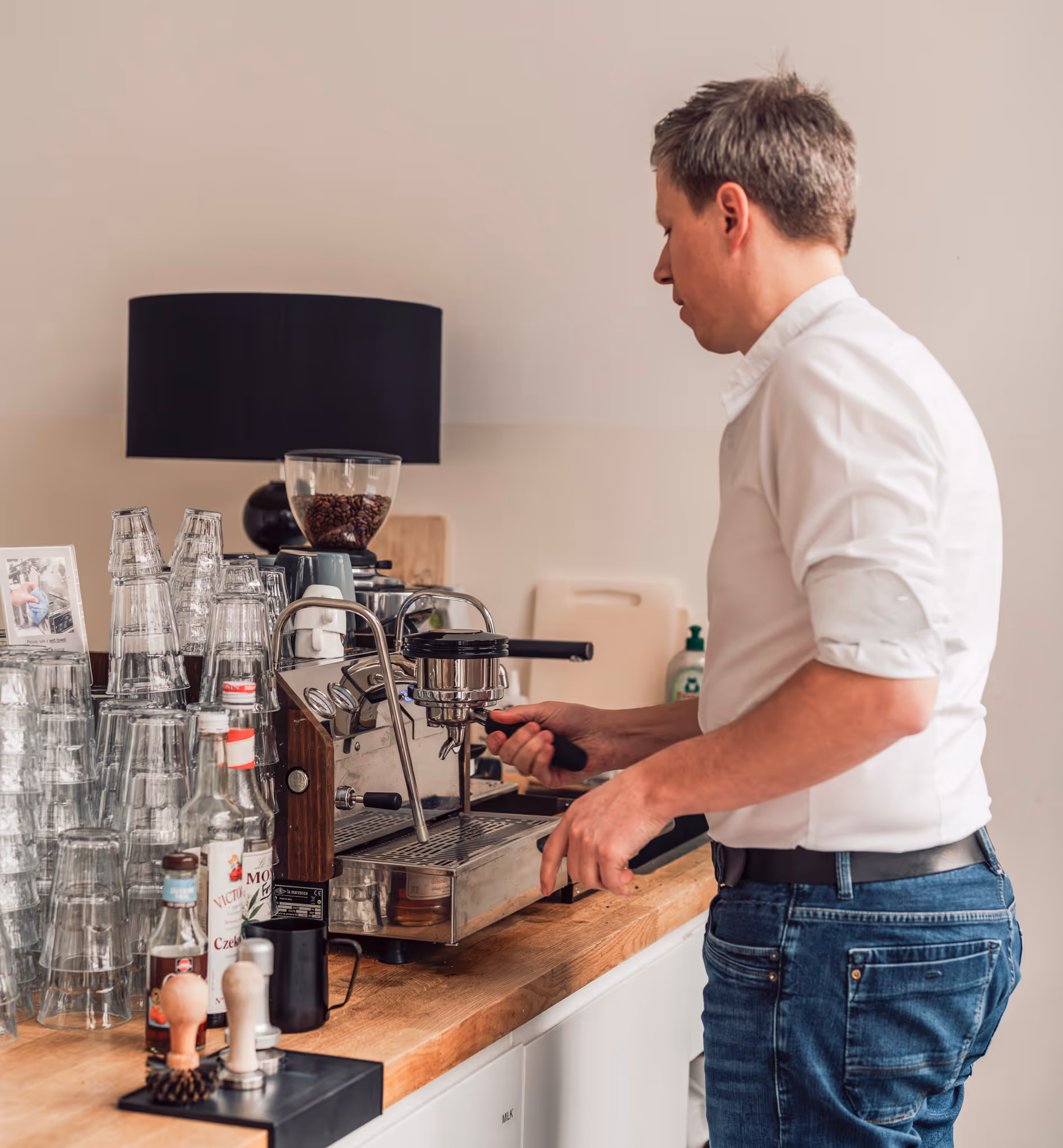 A man in a white shirt is standing in front of a coffee machine.