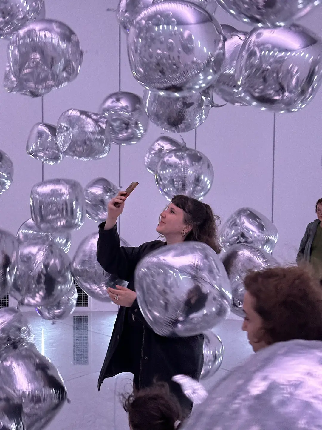 A person excitedly observing modern art installations of floating silver balloons.