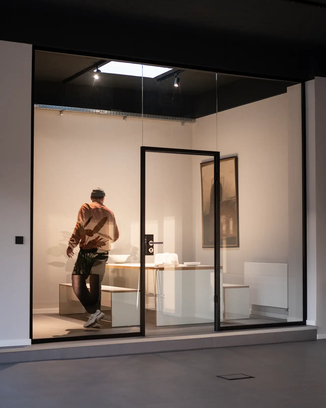 A man standing in a kitchenroom carrying something to the table.