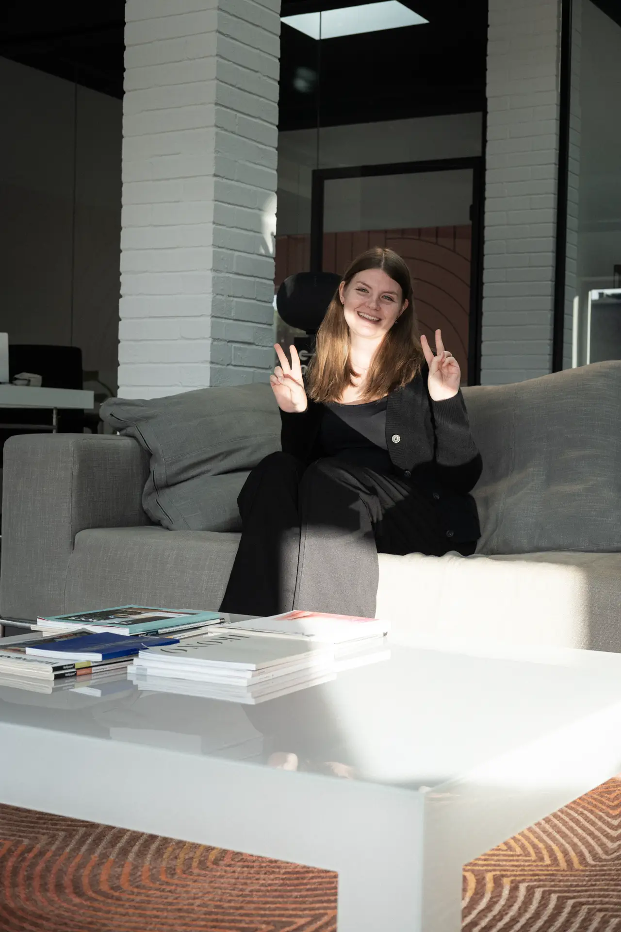 A person smiling and giving a peace sign while sitting on a couch.