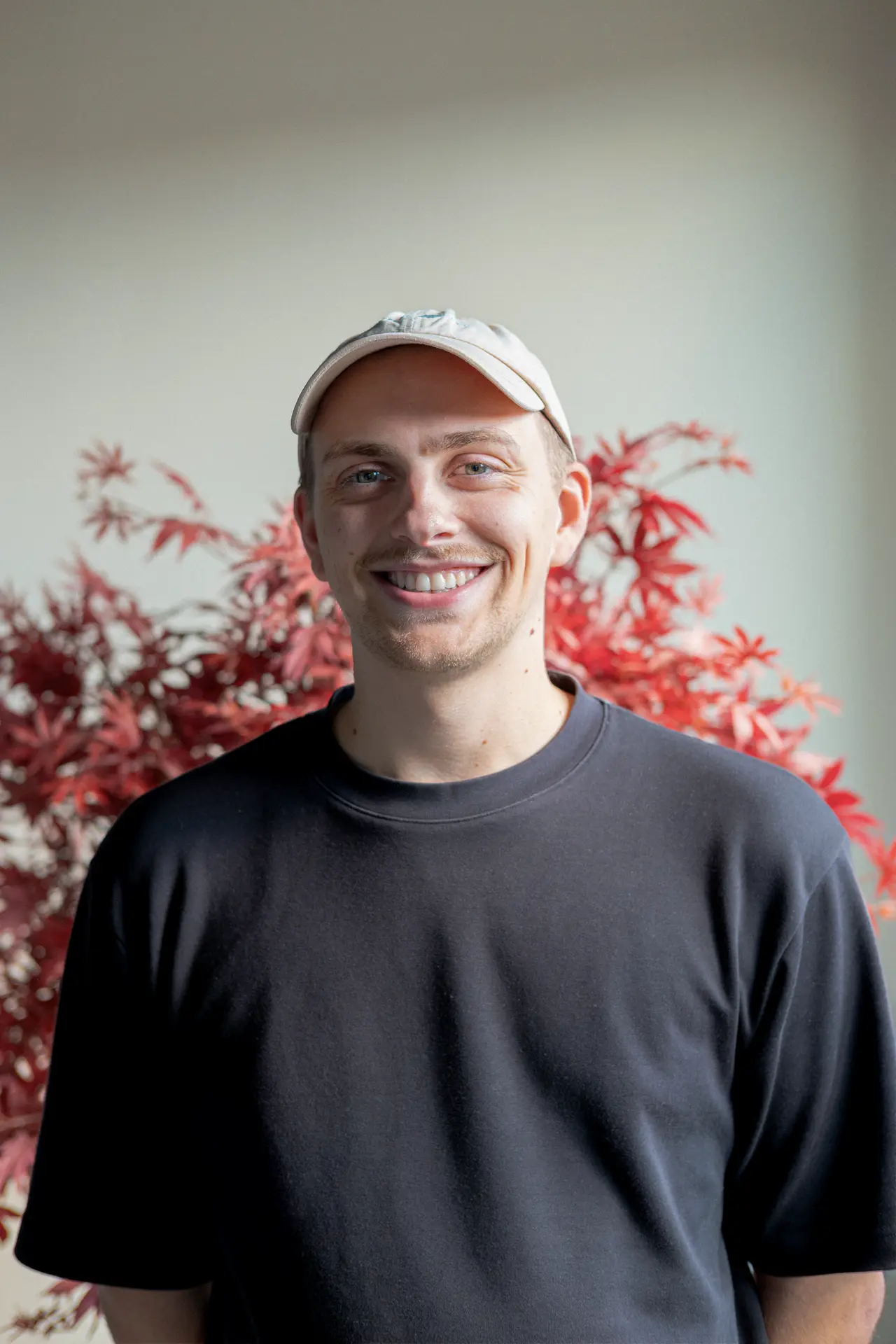 Raphael steht vor einem Ahornbaum und lächelt in die Kamera.