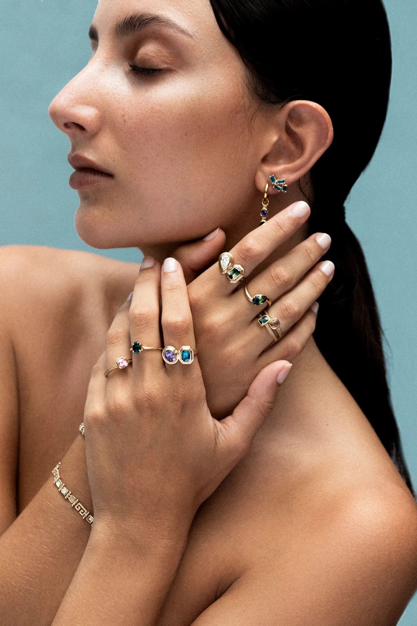 A striking profile image of a model clasping her hands, stacked in colourful costume rings with sapphires, topaz and diamonds.