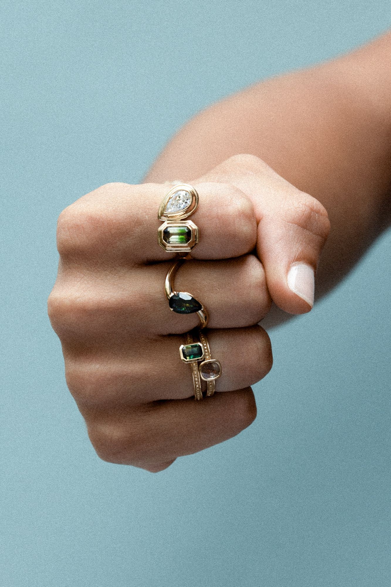 A fist stacked with diamond and sapphire cocktail rings.