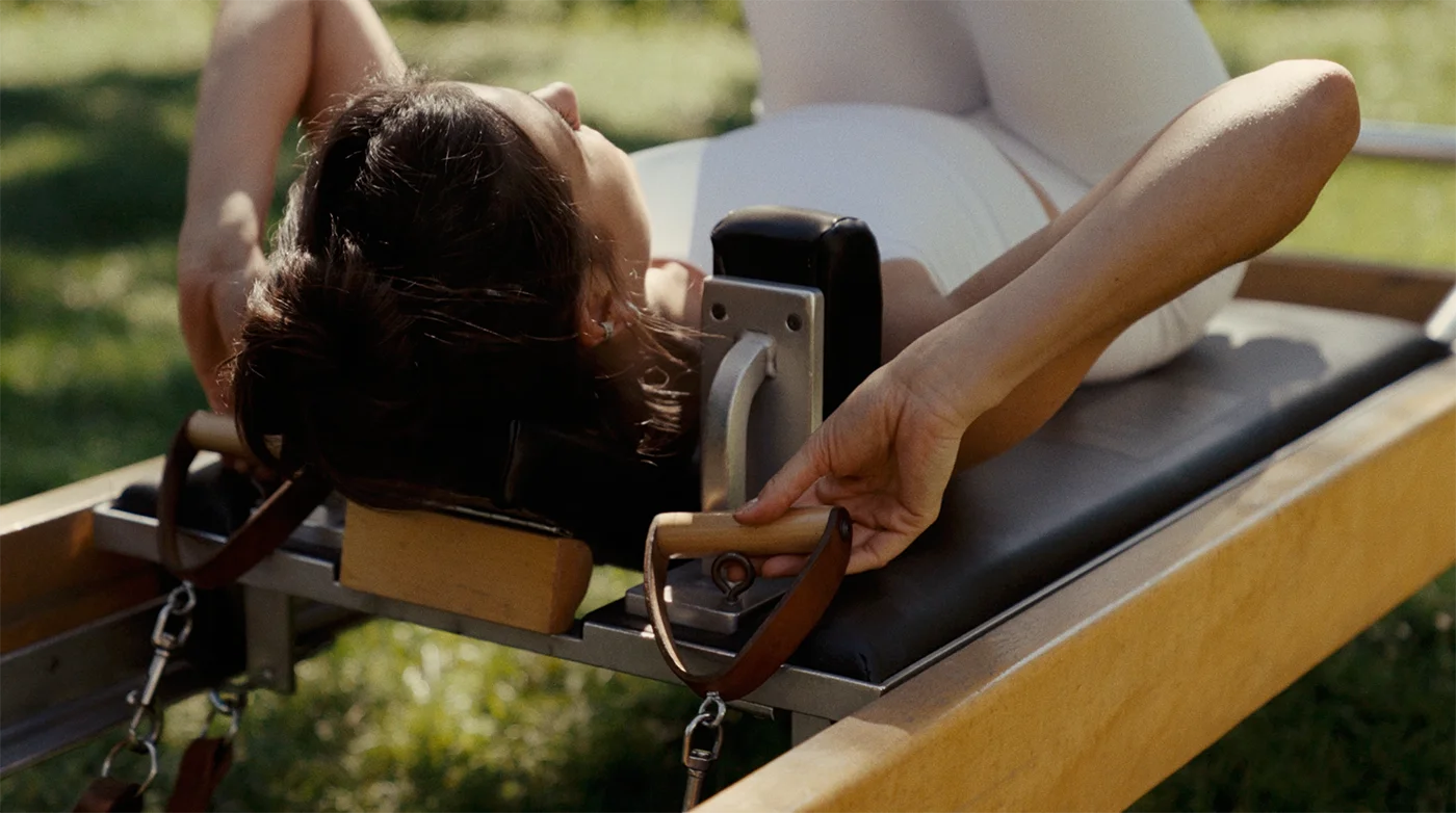 Frau liegt auf einer Pilates-Reformer-Maschine im Freien und hält die Griffe während einer Übung.