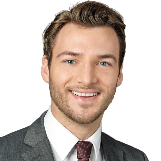 Junger Mann mit braunem Haar, blauem Hemd und grauem Anzug lächelt vor weißem Hintergrund.