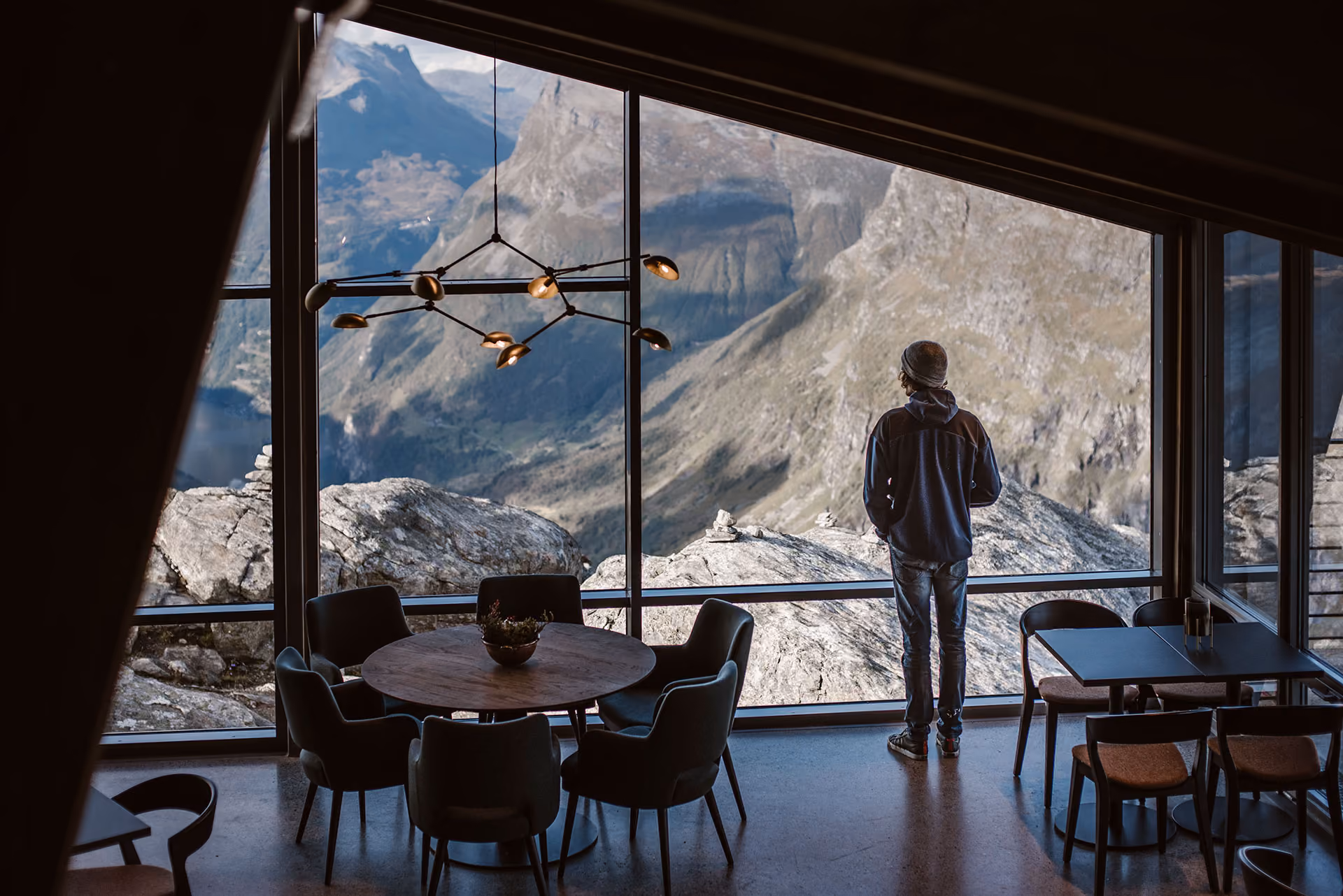 Person standing inside a modern room with large windows overlooking rocky mountains and valleys.