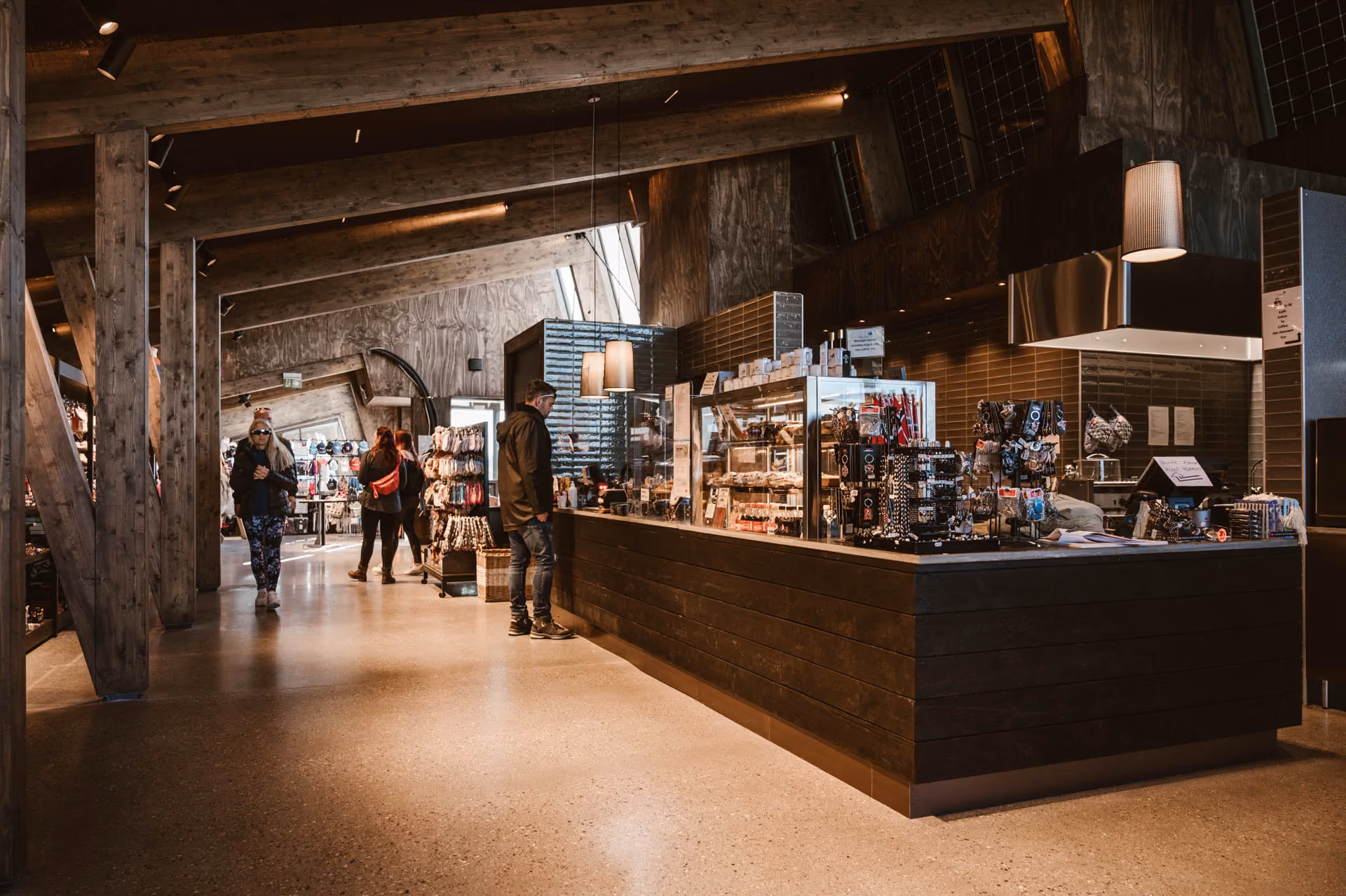 Modern rustic shop interior with wooden beams, a counter displaying snacks and merchandise, and several people browsing.