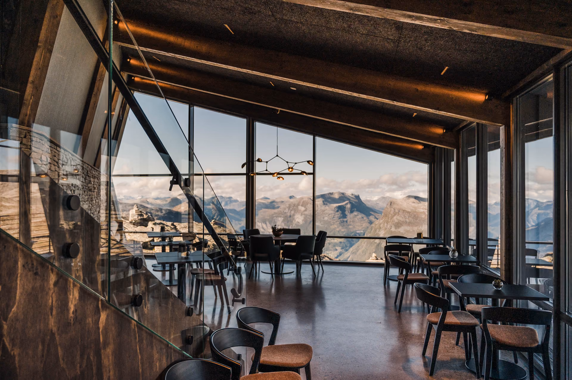 Modern dining area with black chairs and tables inside a glassed room overlooking mountain scenery.