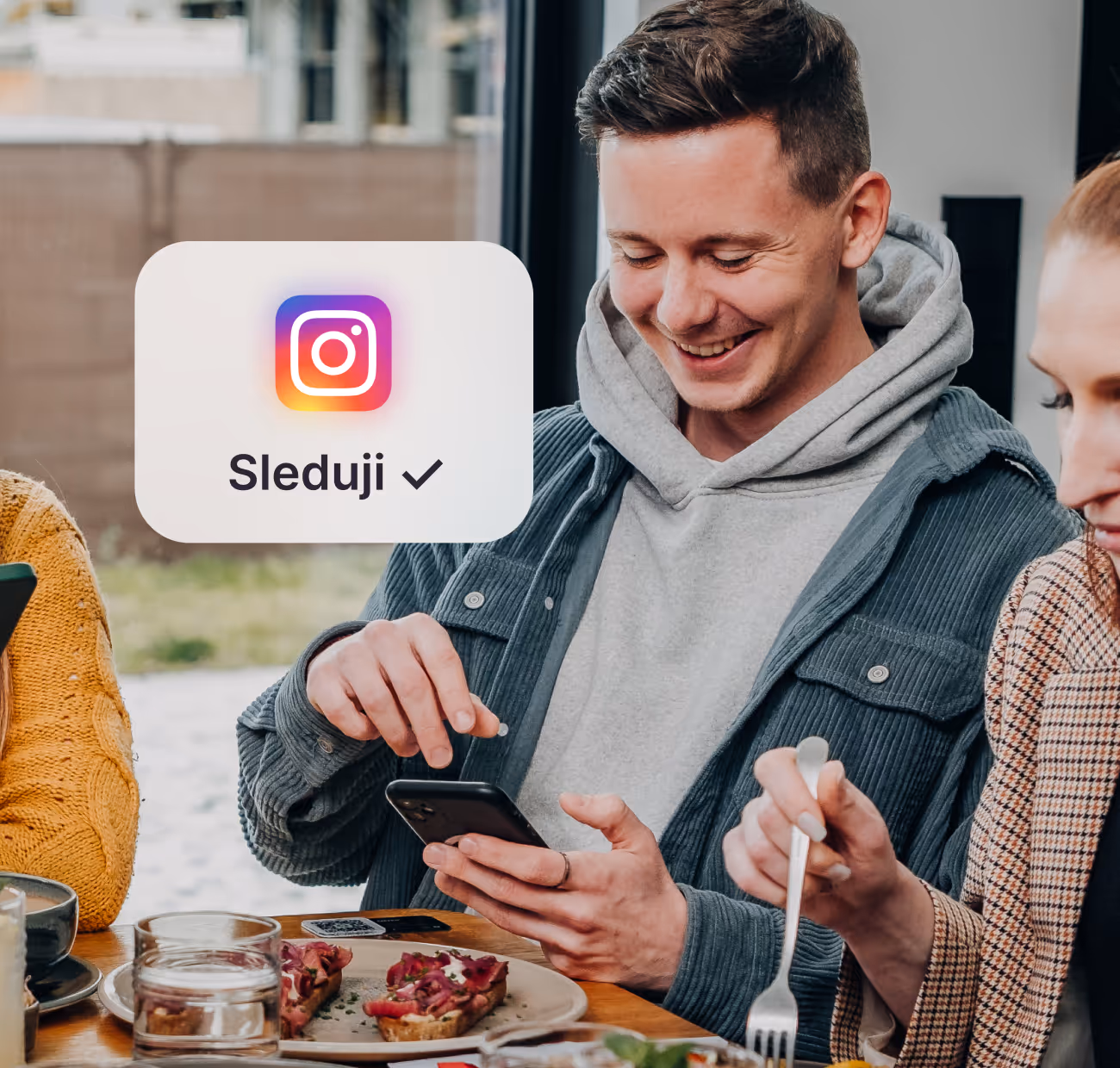 Mladý muž sedí u stolu s jídlem, usmívá se a používá mobilní telefon, vedle je ikonka Instagramu s textem Sleduji a zaškrtnutím.
