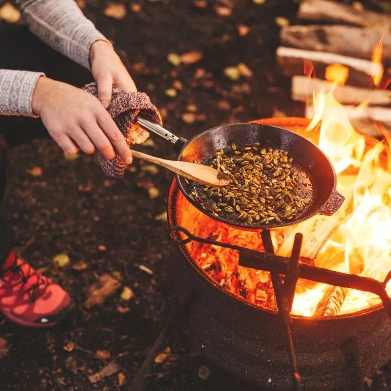 Rustikales Kochen im Wald – Mahlzeit über offenem Feuer zubereitet, umgeben von alten Utensilien und natürlicher Atmosphäre.