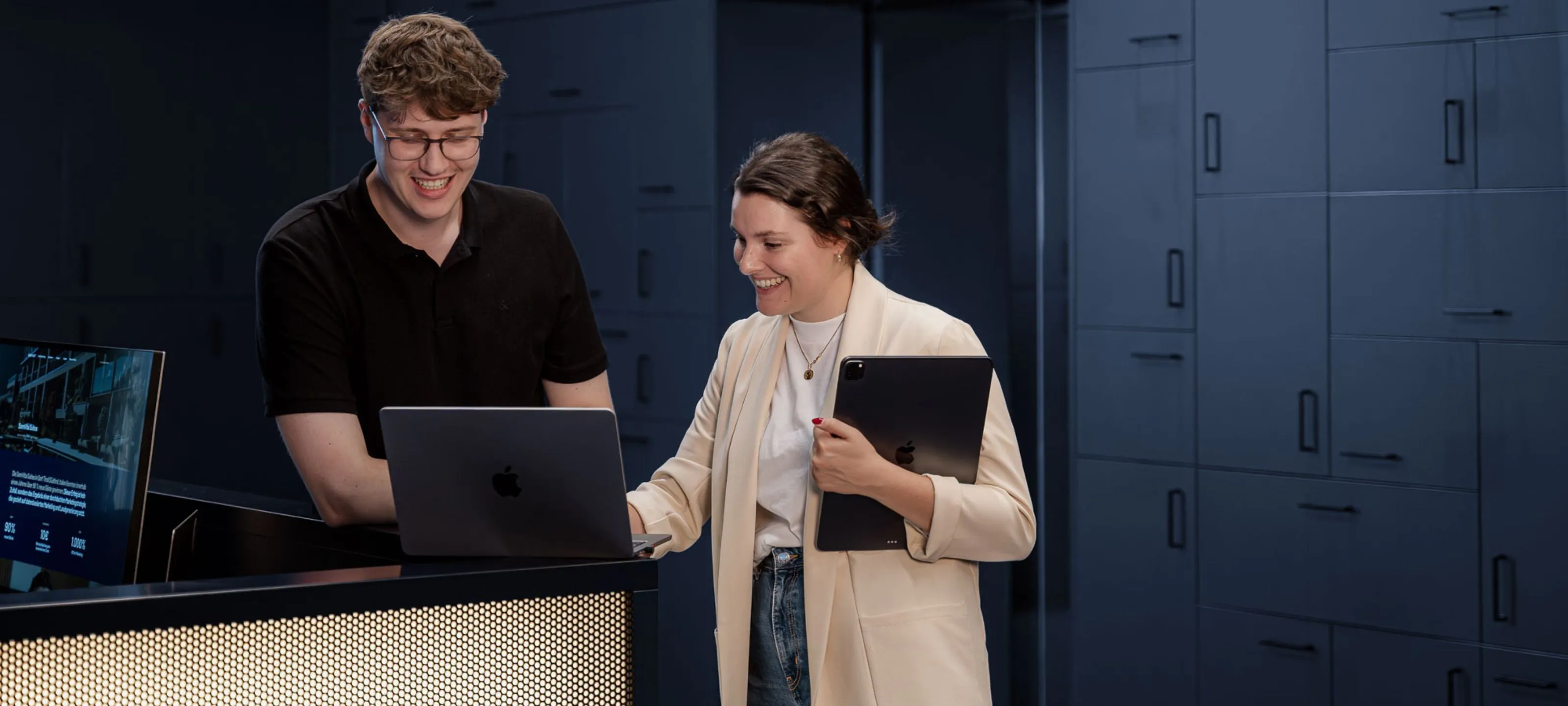 Zwei Mitarbeiter von ADDITIVE schauen auf einen Laptopbildschirm und freuen sich