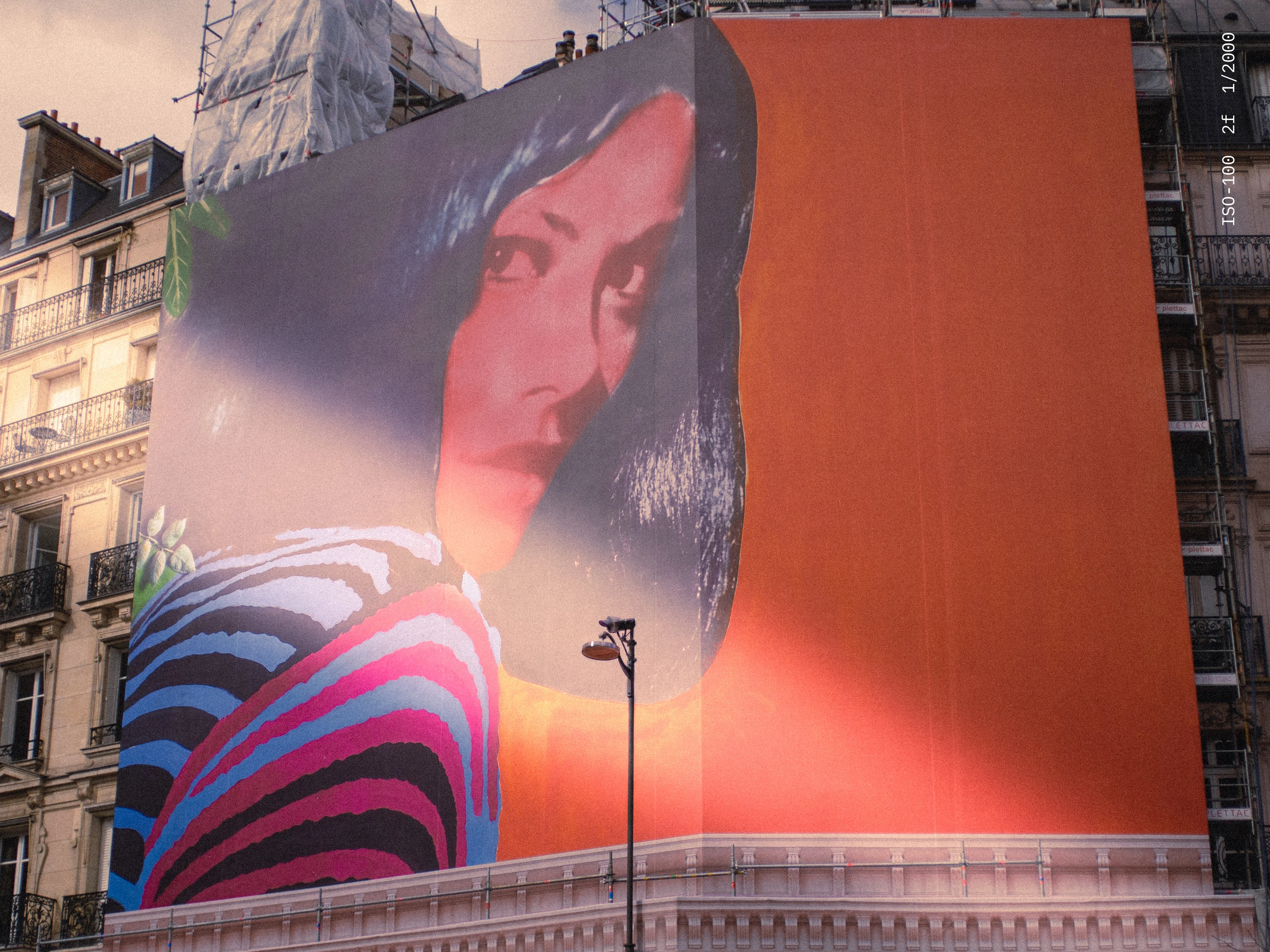 Large mural on building wall depicting a woman with dark hair and a striped garment against an orange background.