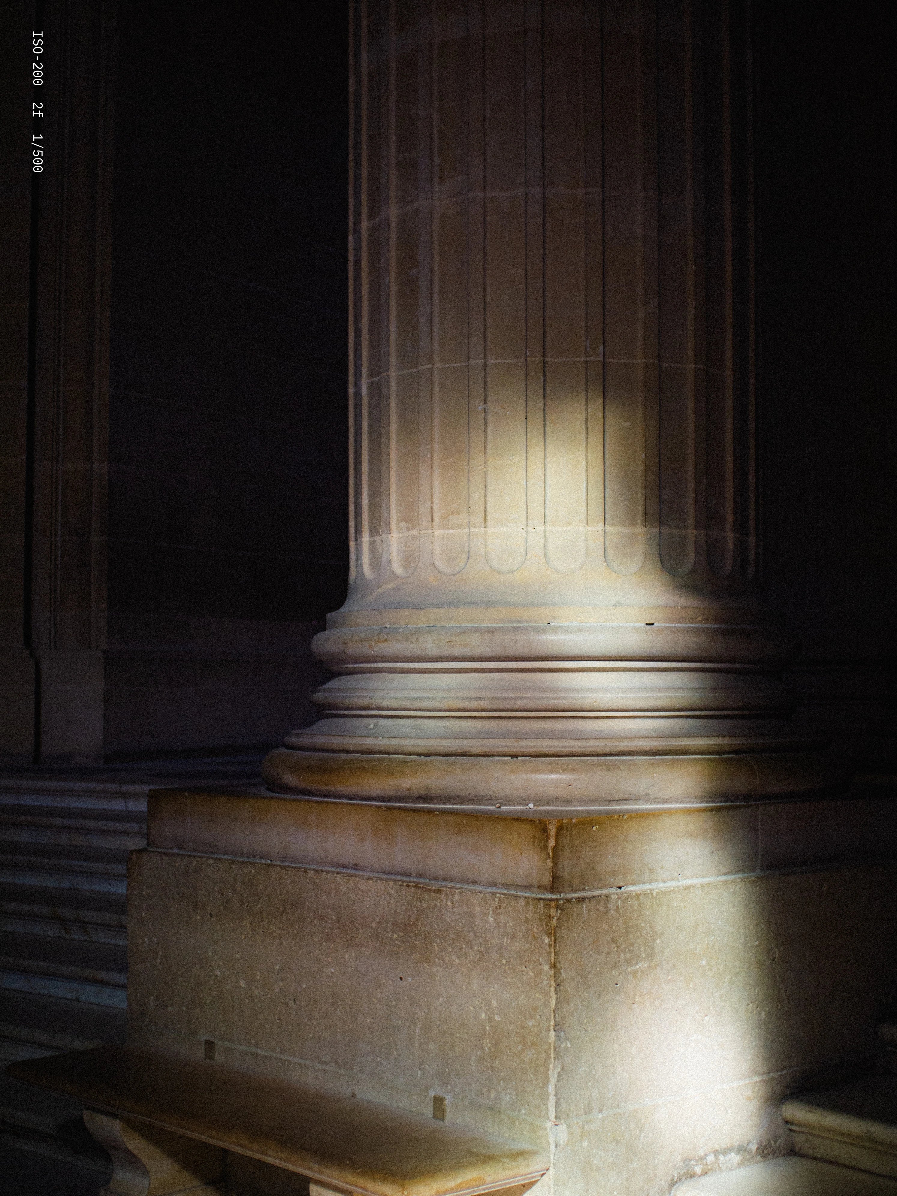 Close-up of a lit classical stone column base with fluted design in a dimly lit interior.