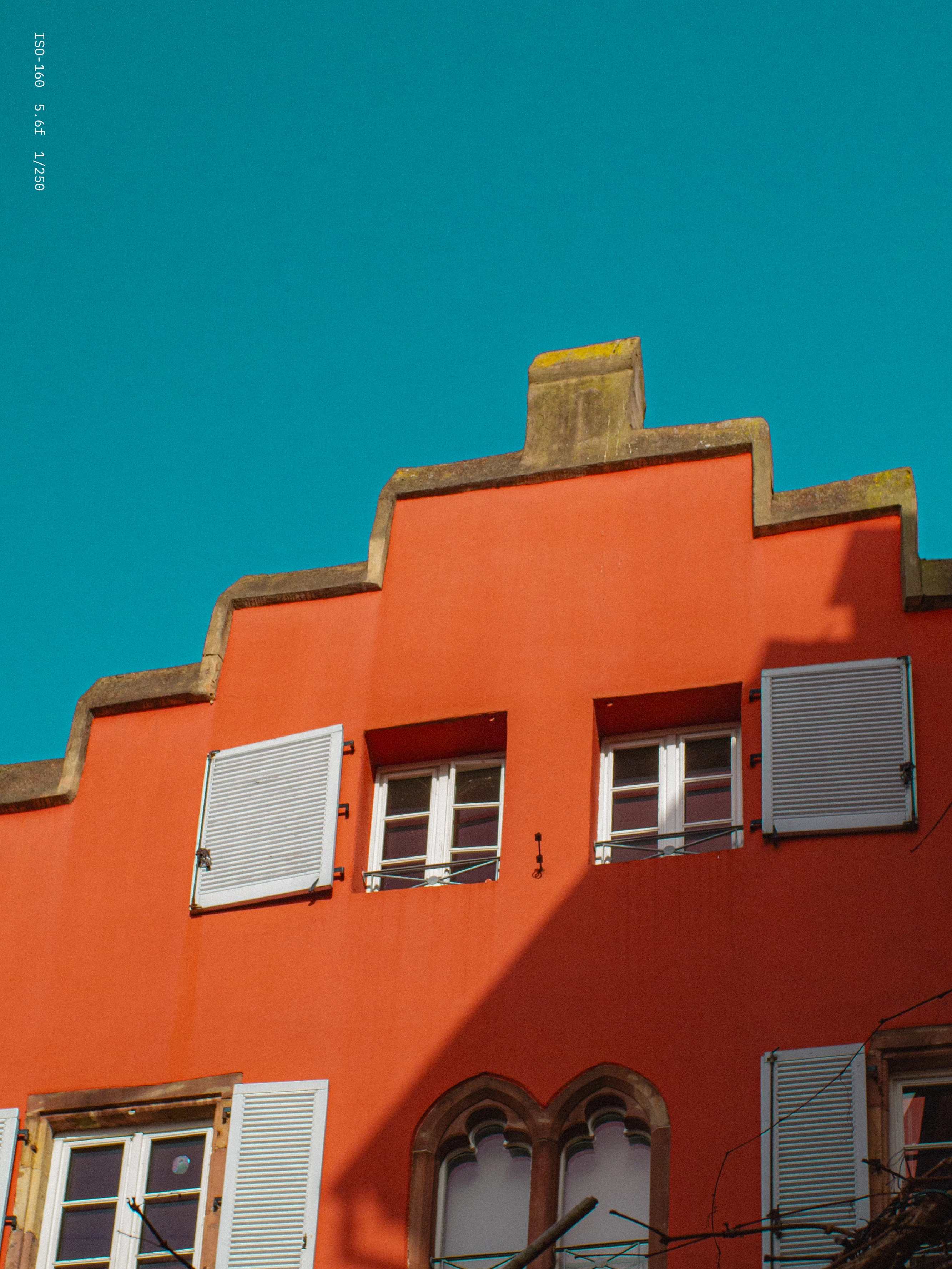 Orange building facade with white shutters on windows and a clear blue sky overhead.