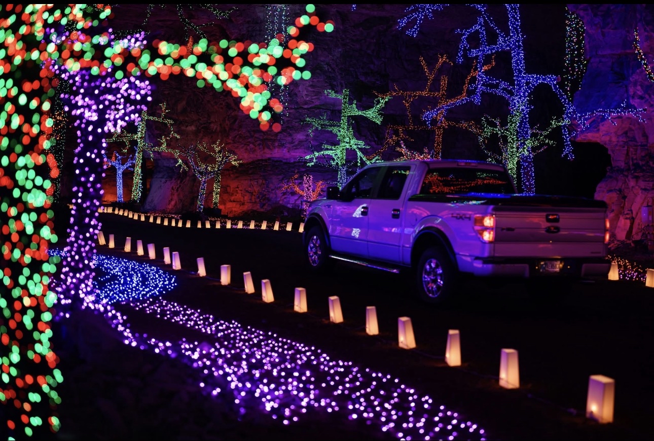 Image Description: A promotional image for Lights Under Louisville at the Louisville Mega Cavern. A truck drives down a pathway in an expansive cavern illuminated by countless Christmas lights.