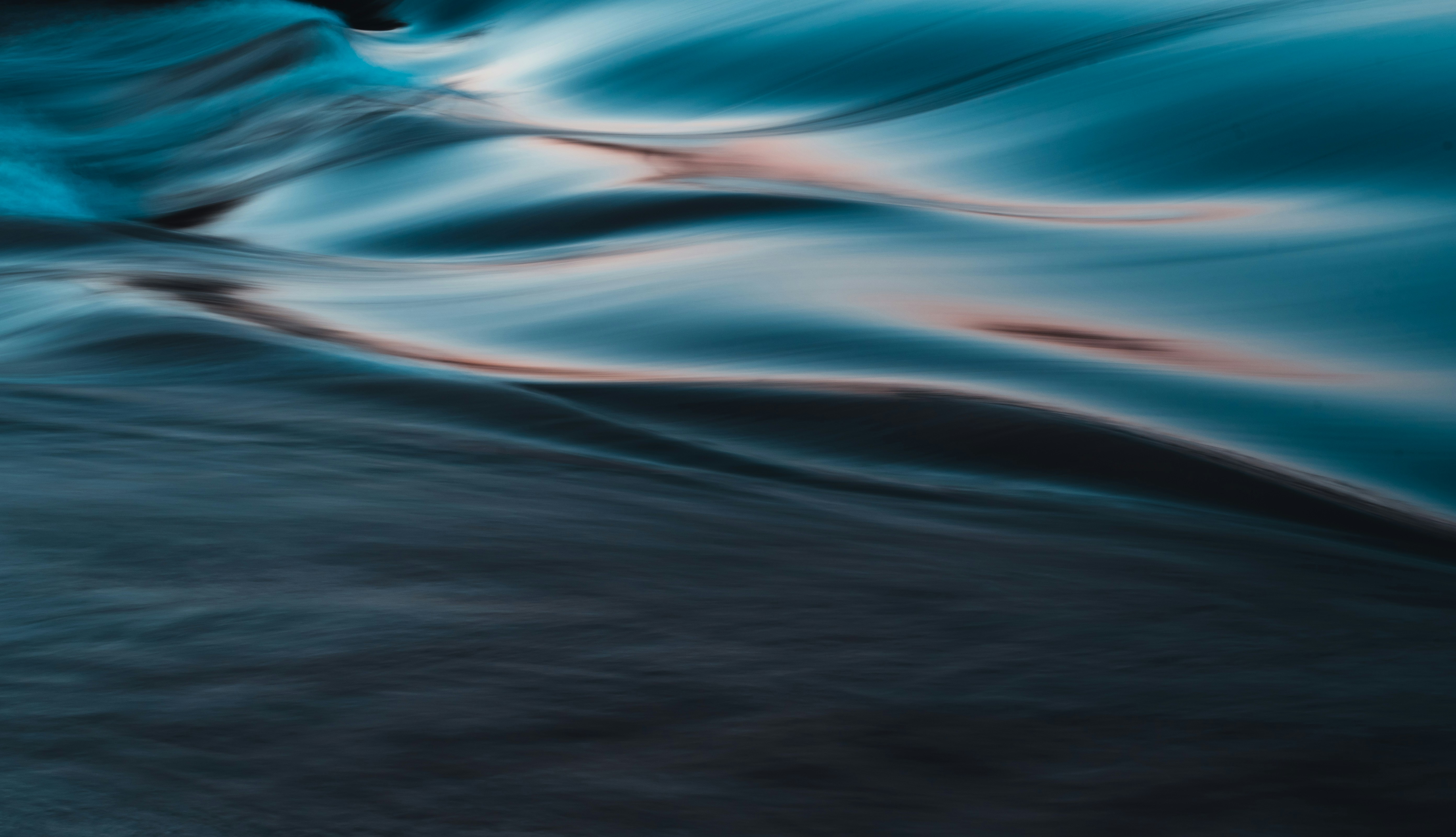 Longue exposition abstraite d'une surface d'eau en mouvement, traînées bleu pétrole, blanches et rosées.