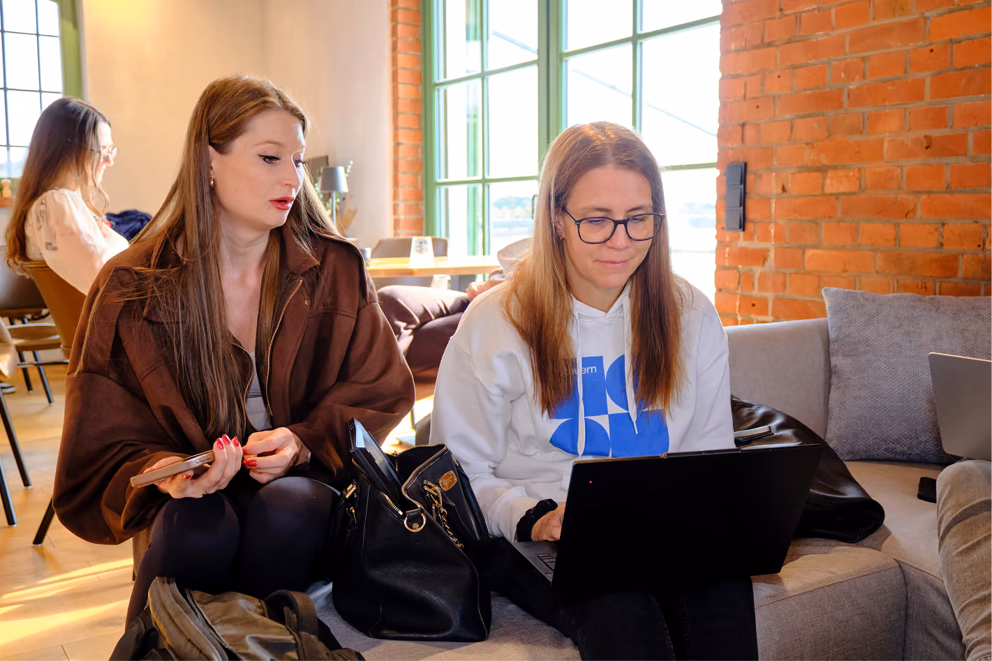 Zwei Kolleginnen arbeiten gemeinsam am Laptop auf dem Sofa