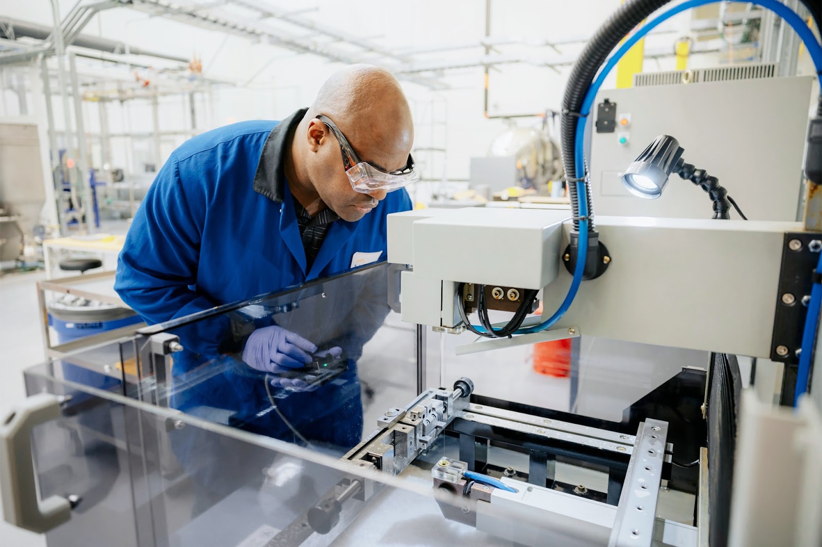 A man working in a lab. He's wearing a blue coat, gloves and safety glasses.