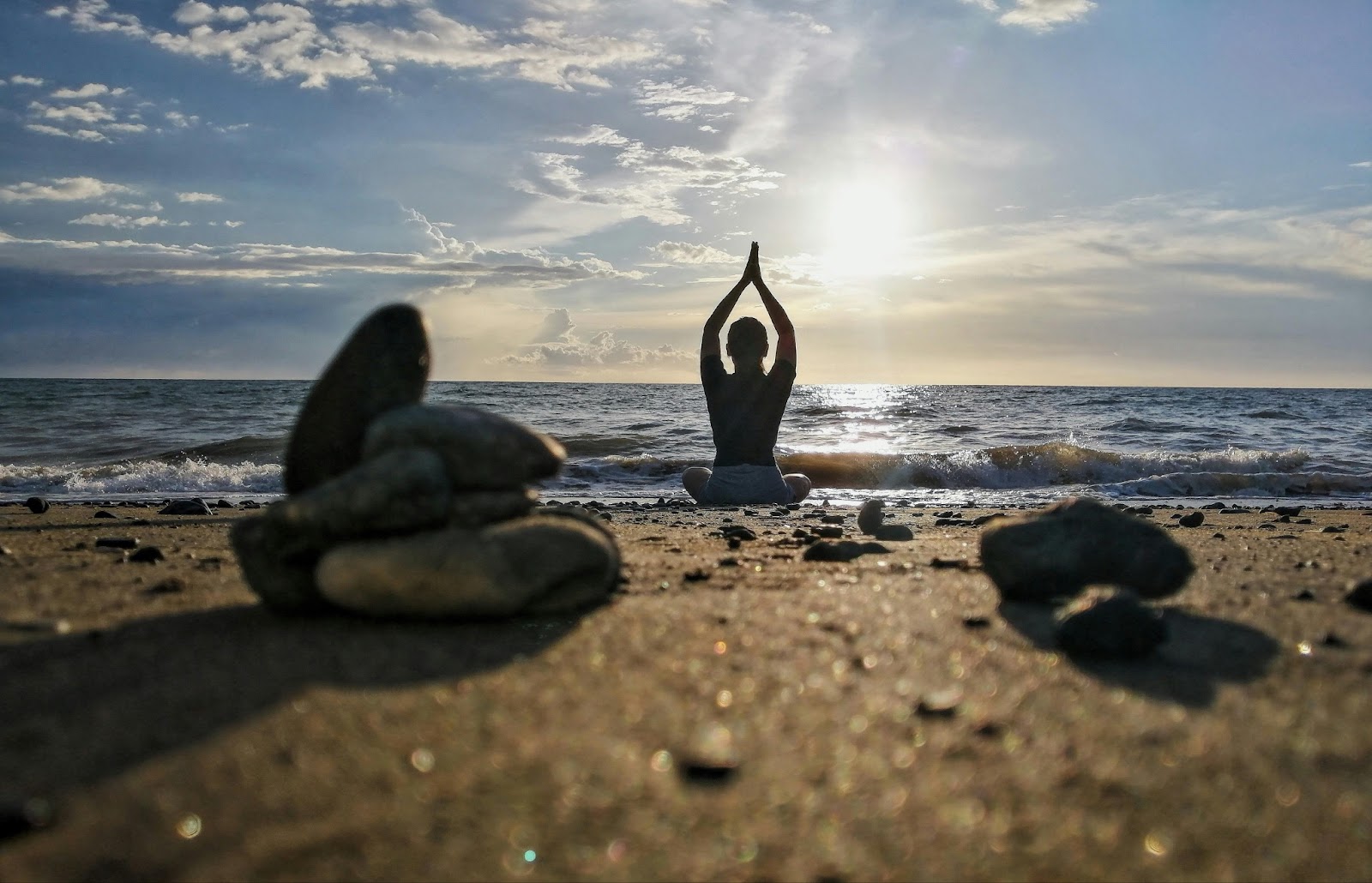 A person sitting on the beach facing the sea, there are small rocks on the sand.