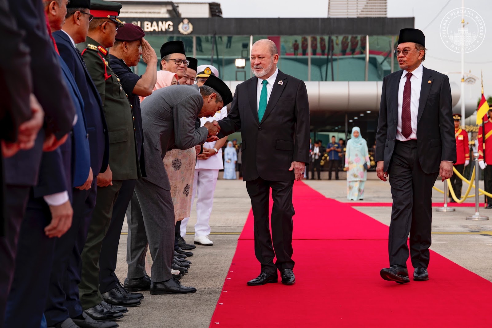Yang di Pertuan Agong (King of Malaysia on a red carpet by a line being greeted by a line of official, Malaysia Prime Minister, Anwar Ibrahim, standing next to him