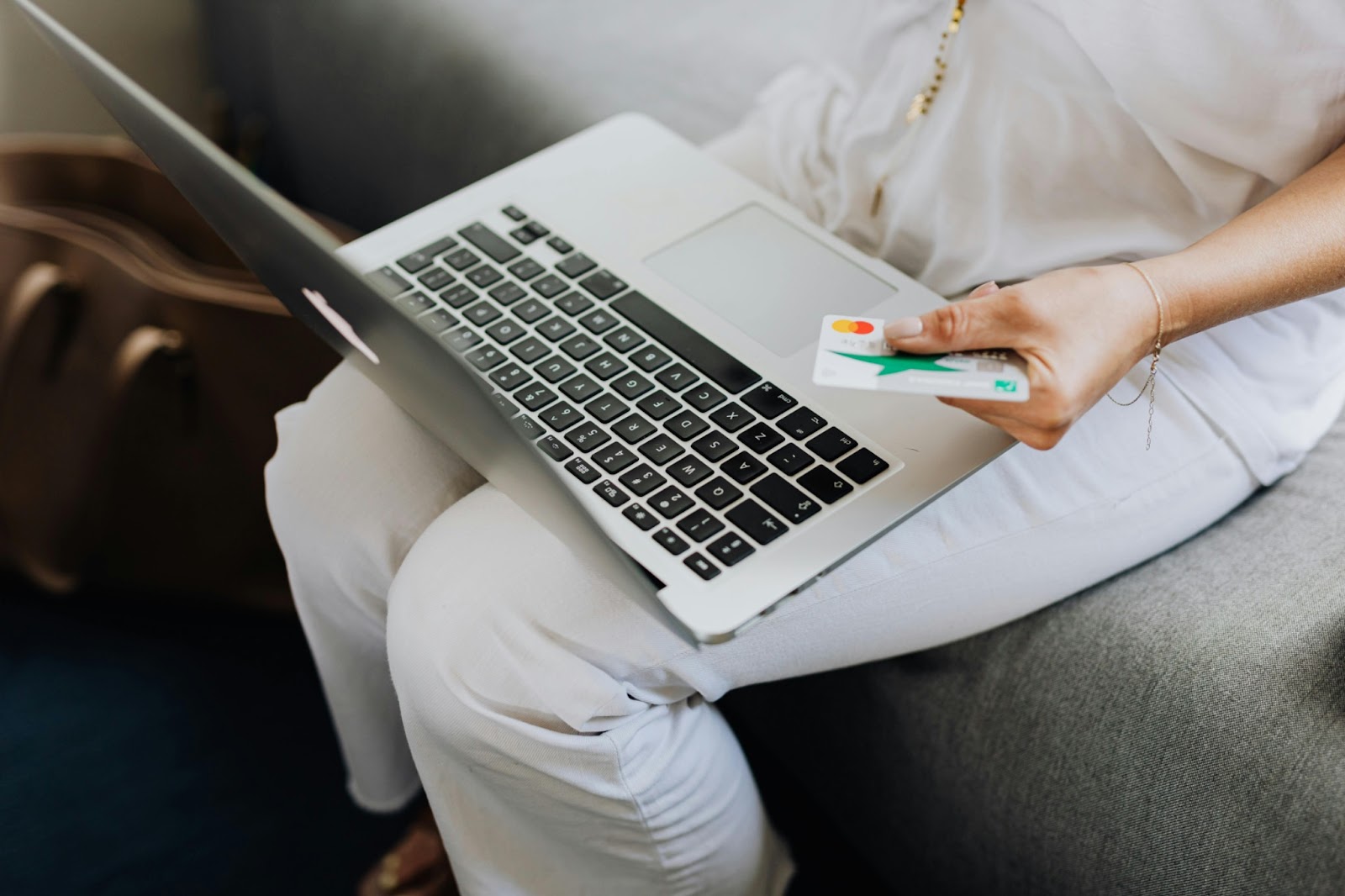 A woman is holding a debit card and a macbook on her lap