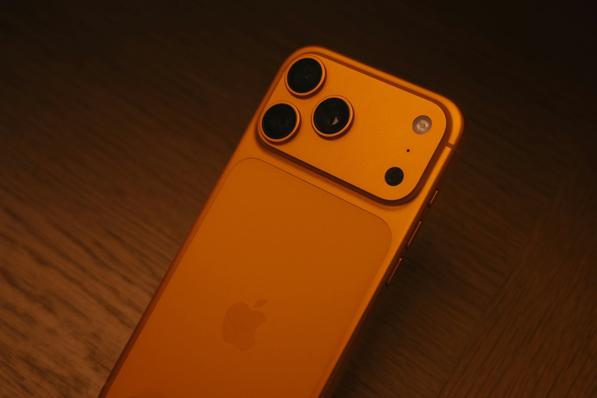 iPhone 17 Pro Max in orange with triple-lens camera, shot in warm lighting with a sleek, premium look.