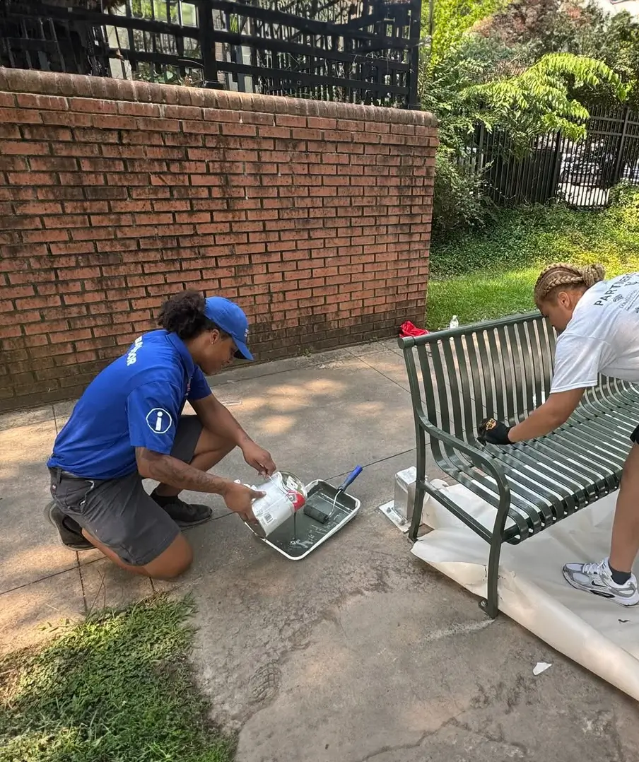 A Downtown Ambassador pours paint for repainting a bench downtown