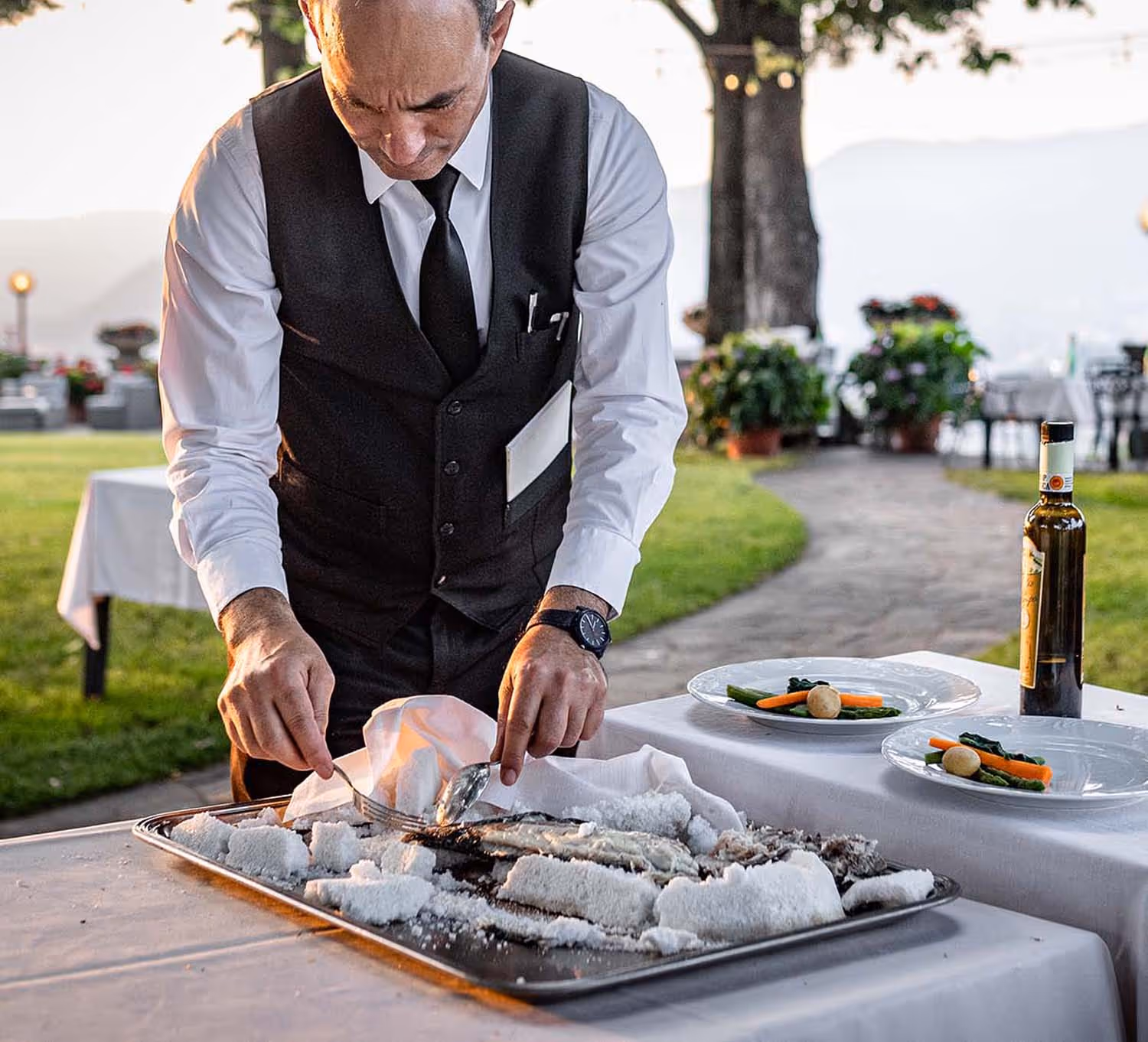 Cameriere che taglia del branzino al sale in giardino