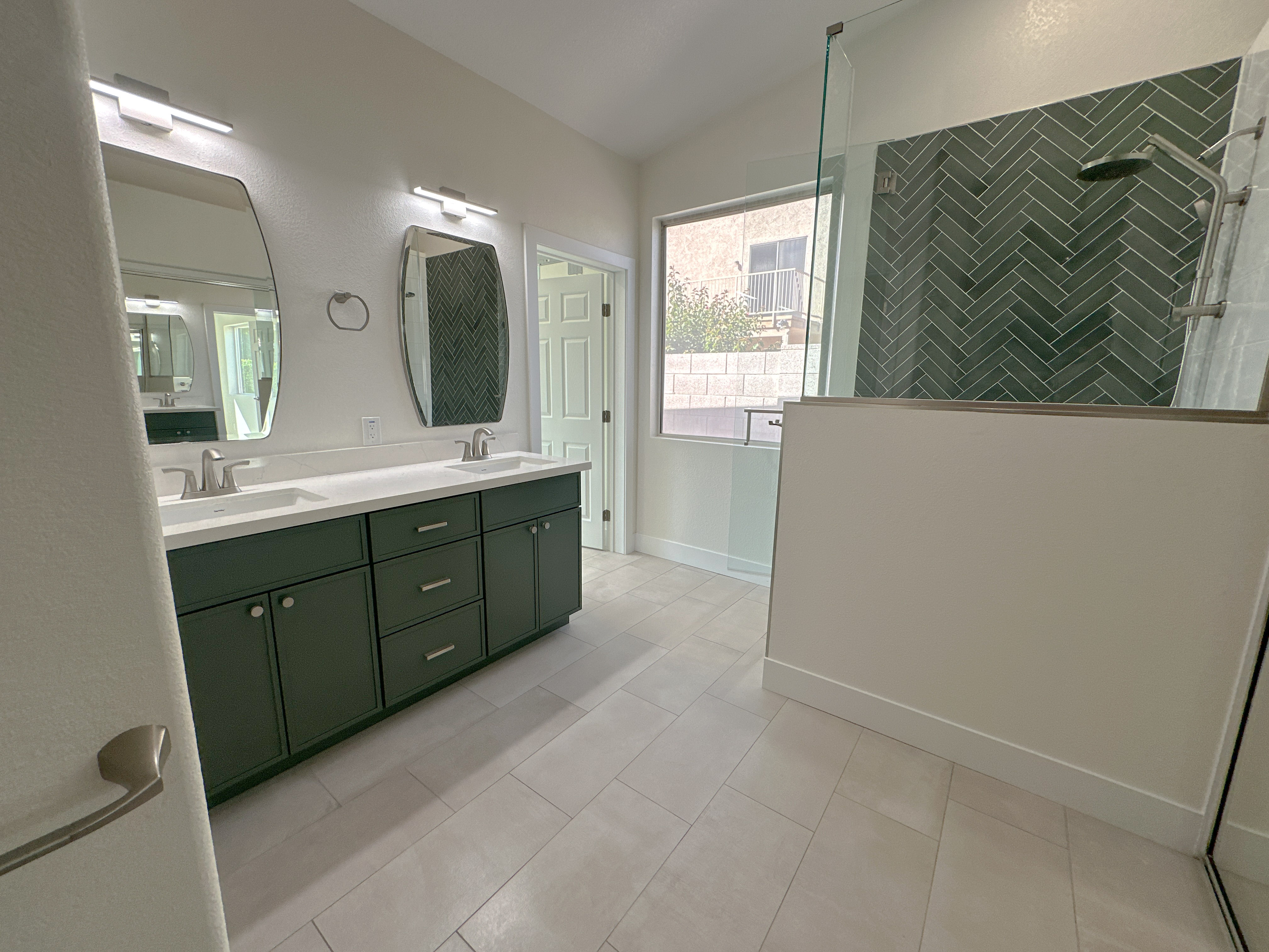A picture of the Hess bathroom remodel. Green cabinets and shower tiles paired with white and silver countertop and adornments.