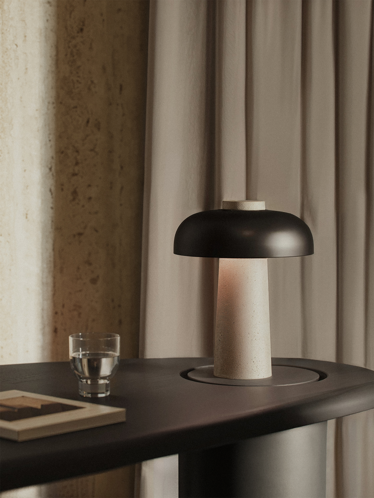 “Modern table lamp with ceramic base and matte black dome shade on sculptural dark desk — minimalist lighting design in soft natural interior