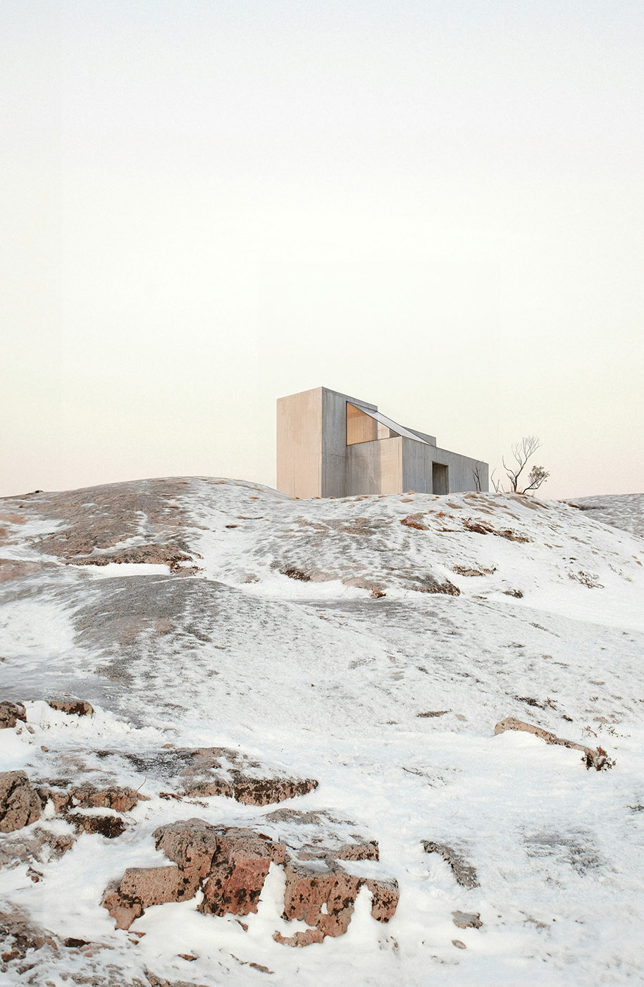 Minimalist cabin in a snowy rocky landscape — concrete and wood architecture blending into a serene winter environment