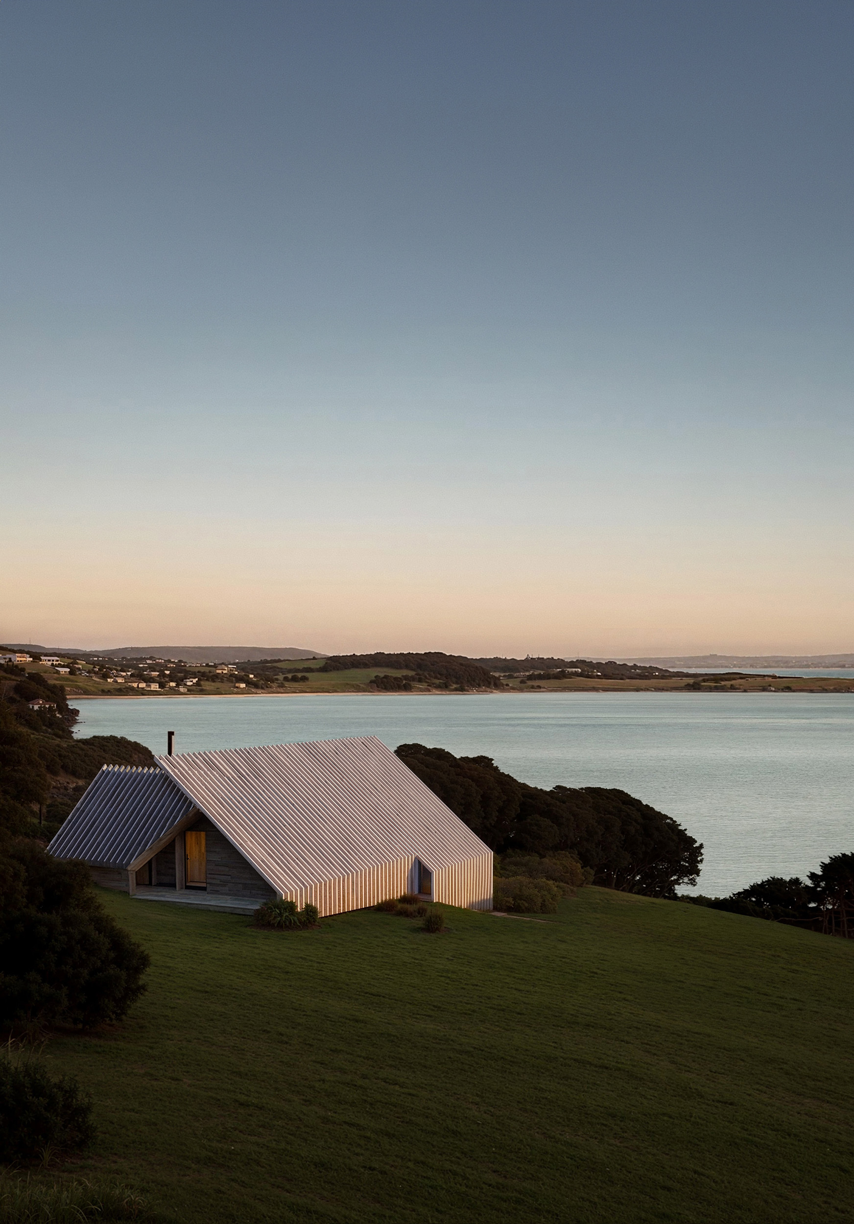 Modern wooden cabin with pitched metal roof overlooking a coastal landscape — contemporary architectural design in nature for remote getaway or sustainable living