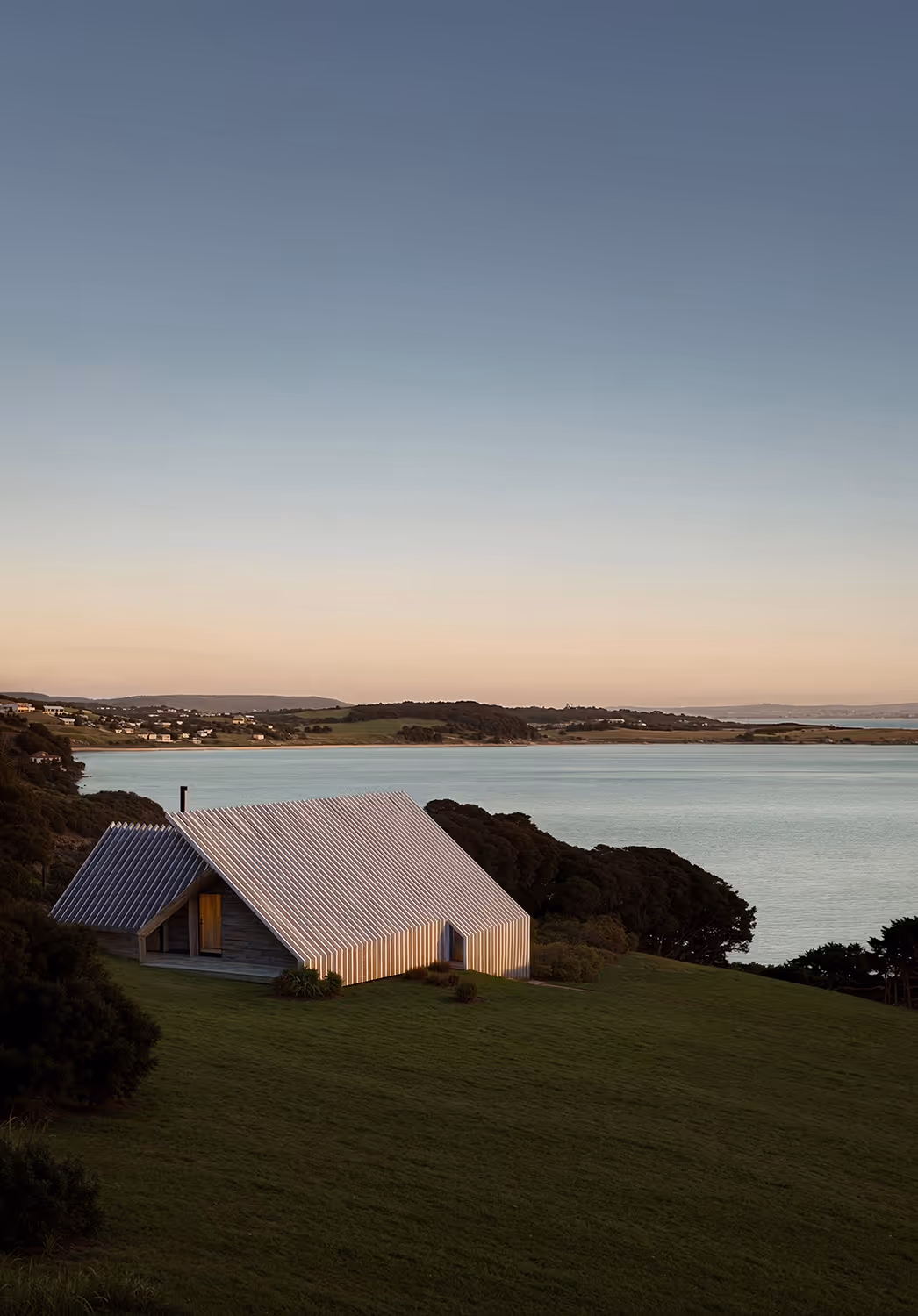 Modern wooden cabin with pitched metal roof overlooking a coastal landscape — contemporary architectural design in nature for remote getaway or sustainable living