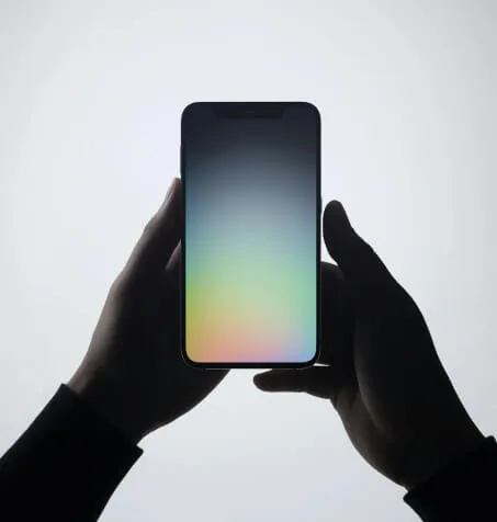 Silhouetted hands holding a smartphone with a glowing gradient screen against a light background.