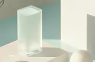 Translucent rectangular glass block casting soft shadows on a white surface against a muted blue and beige background.