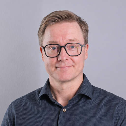 Hymyilevä mies liikemiespuku ja solmio tummaa taustaa vasten.