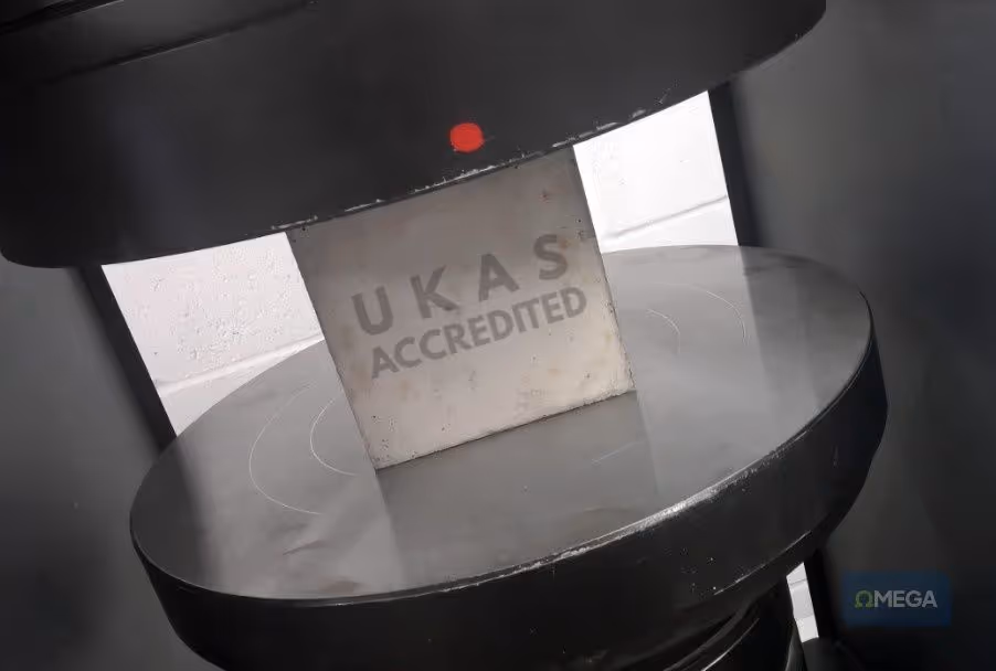 A black industrial compression machine with a cube sample overlayed with "UKAS Accredited." The setting is industrial, with a focus on precision, authority, and credibility.