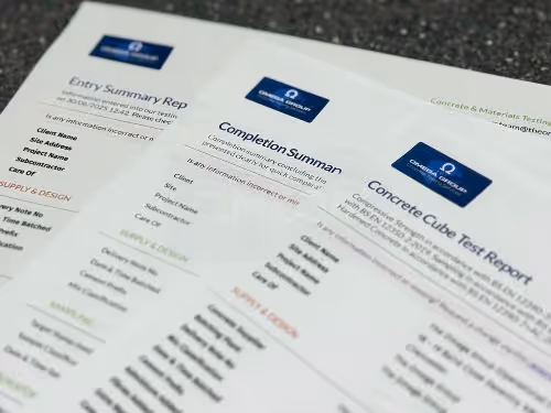 Three printed test reports are spread out on a desk. The visible titles are Entry, Completion, and Concrete Cube Test Report.