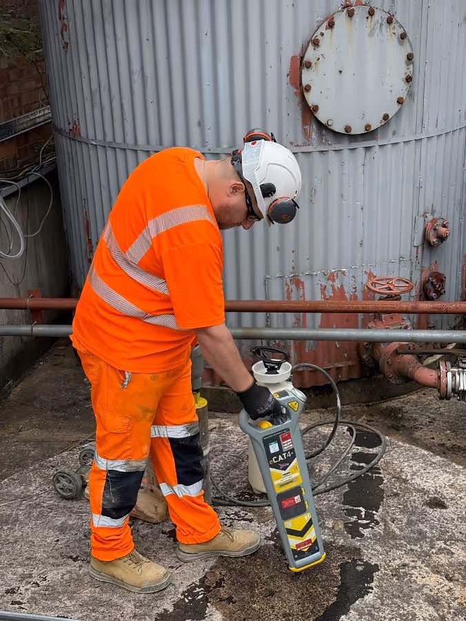 Worker in orange safety gear and white helmet operating a diamond drill on an industrial floor.