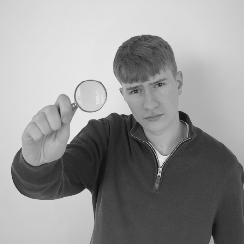 Alfie Madden, an independent SEO consultant, wearing a quarter zip holding a magnifying glass