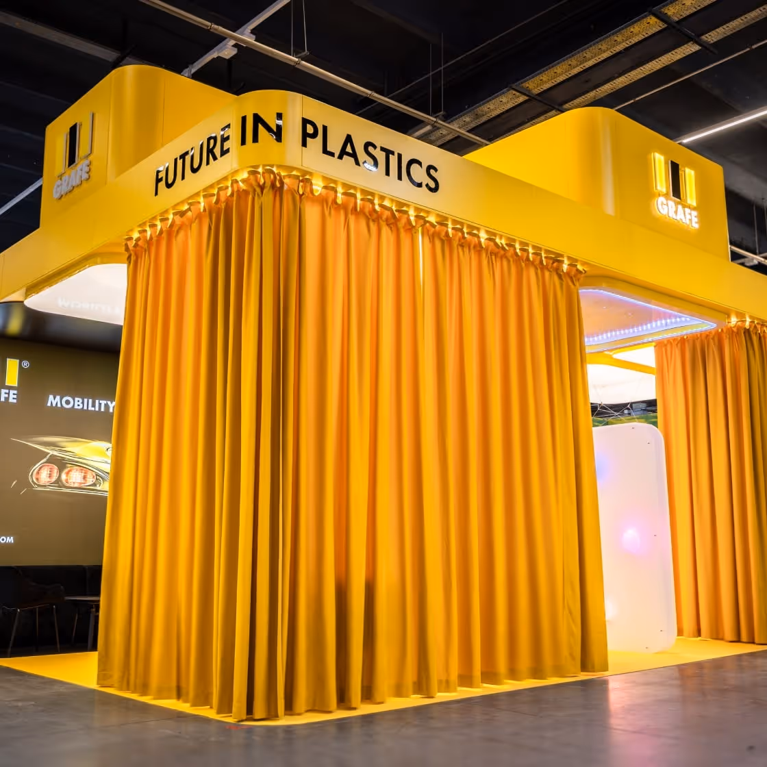 Stoisko targowe z żółtymi zasłonami, logo i napisem "Future in Plastics".