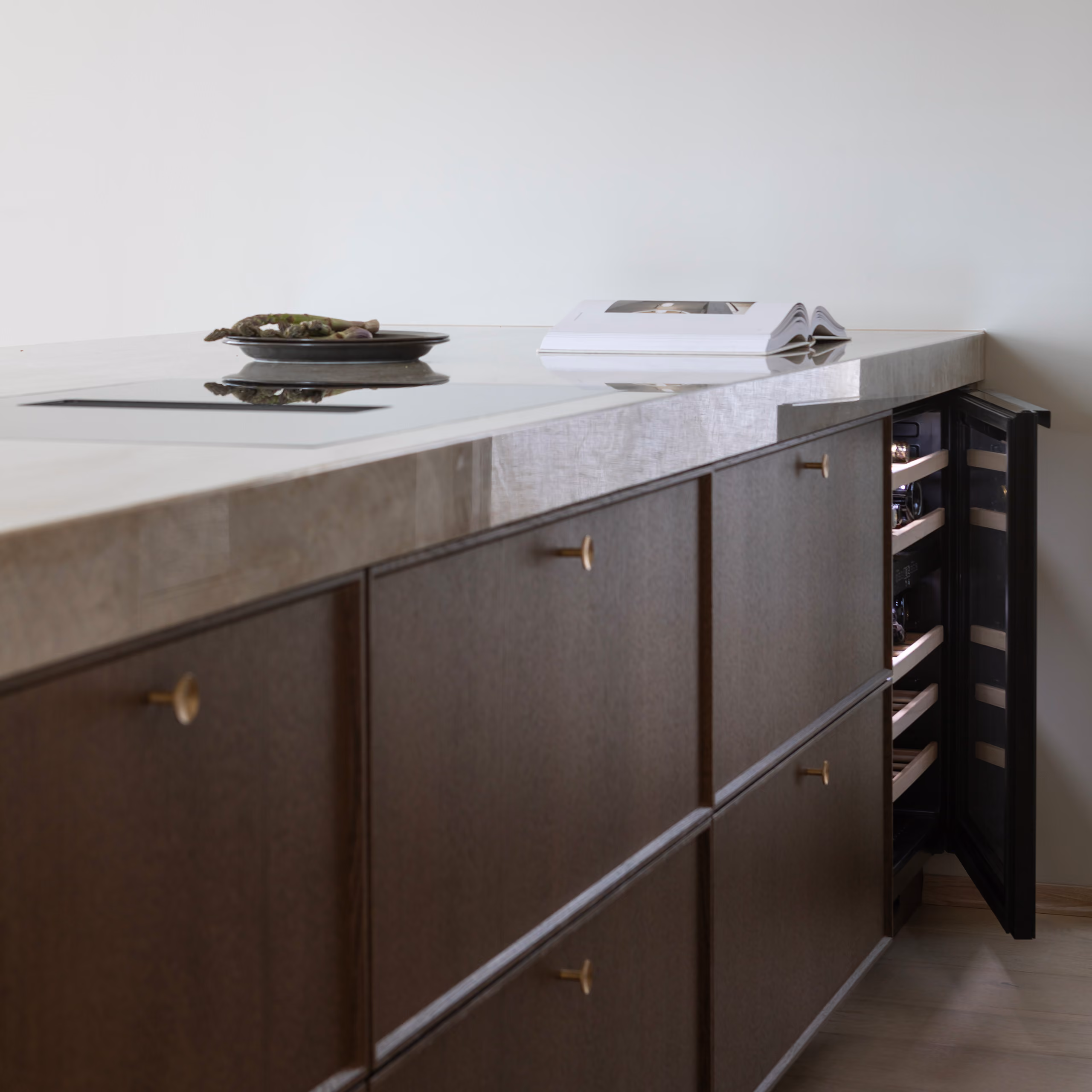 Moderne kjøkkenøy med mørke skuffer og messinghåndtak. Et Norcool vinskap er åpent til høyre.