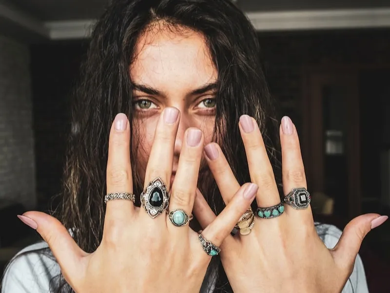 Woman with green eyes shows hands adorned with various decorative rings.