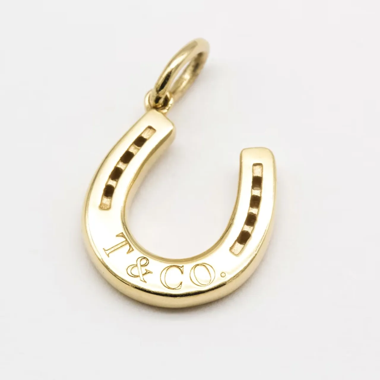 Gold horseshoe pendant engraved with T&CO on a white background.