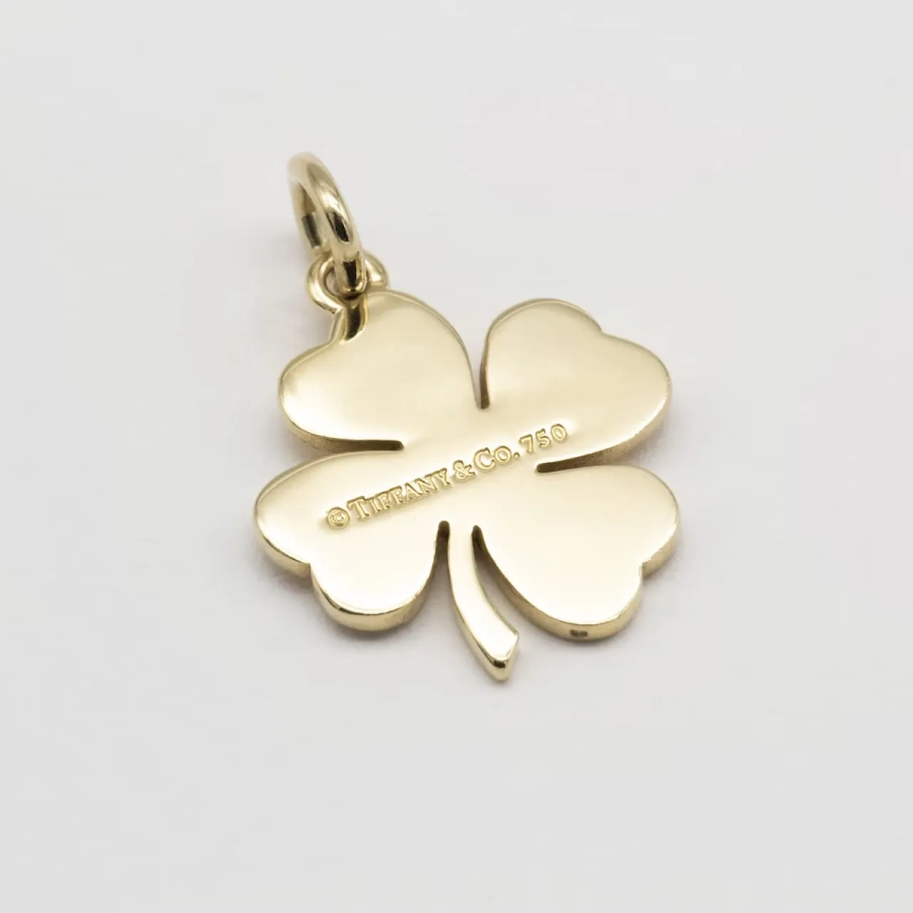 Gold four-leaf clover charm engraved with Tiffany & Co. 750 hallmark on white background.
