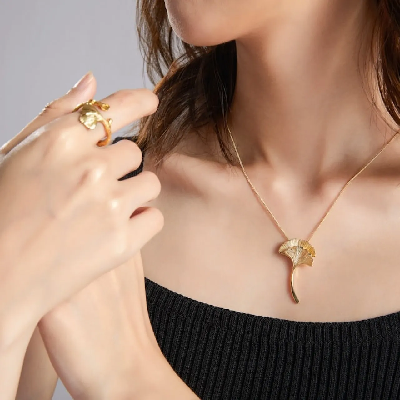 Woman wearing gold ginkgo leaf pendant necklace and matching gold ring on middle finger.