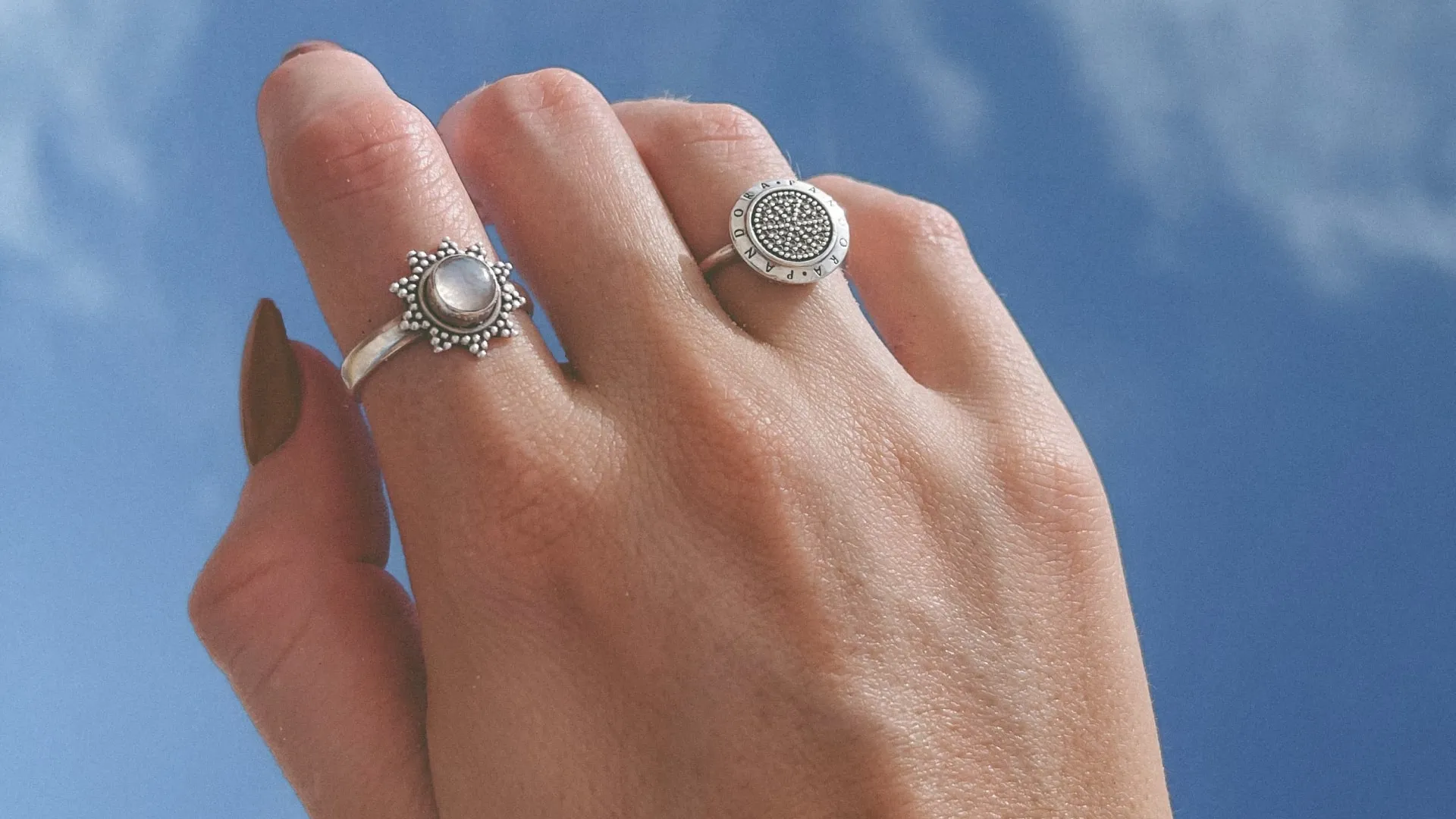 Hand with two silver rings, one with a round gem and the other with small beads and engraved letters.