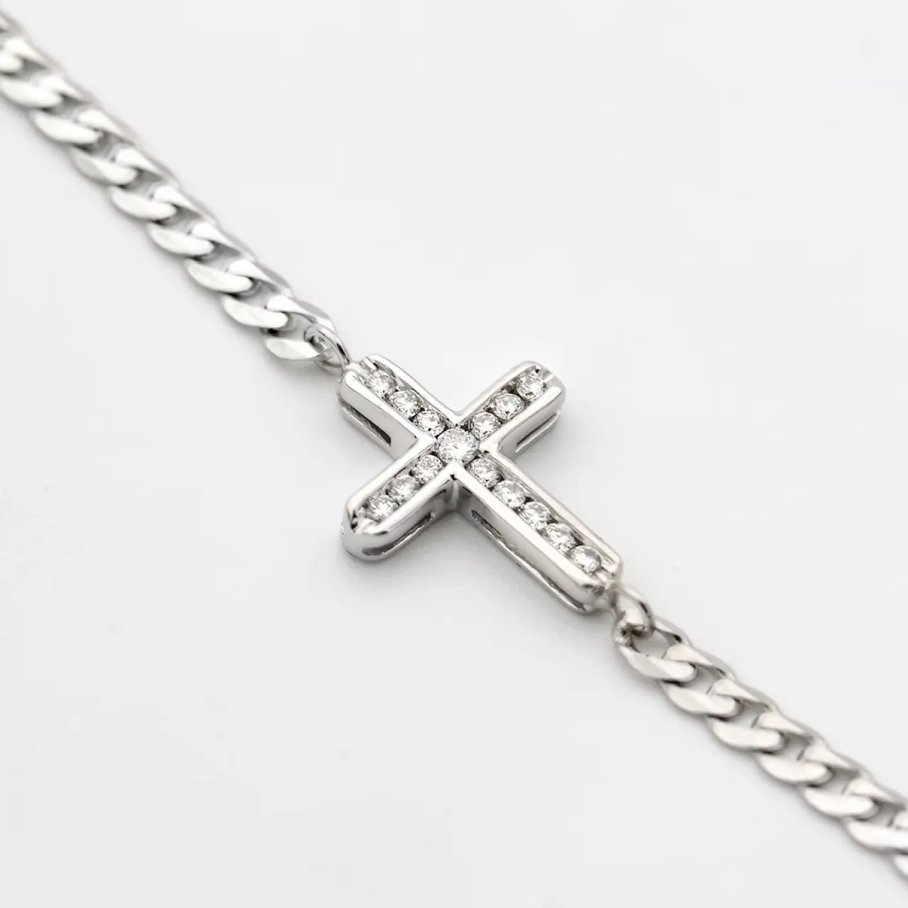 Silver chain bracelet with a cross pendant adorned with small clear gemstones.