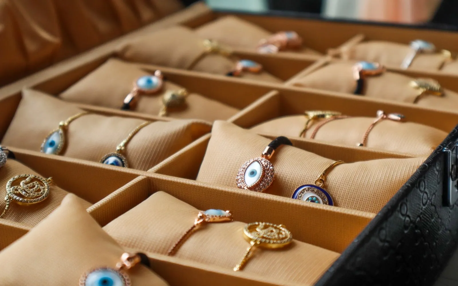 Tray with beige cushions holding gold and rose gold bracelets with blue eye-shaped charms.