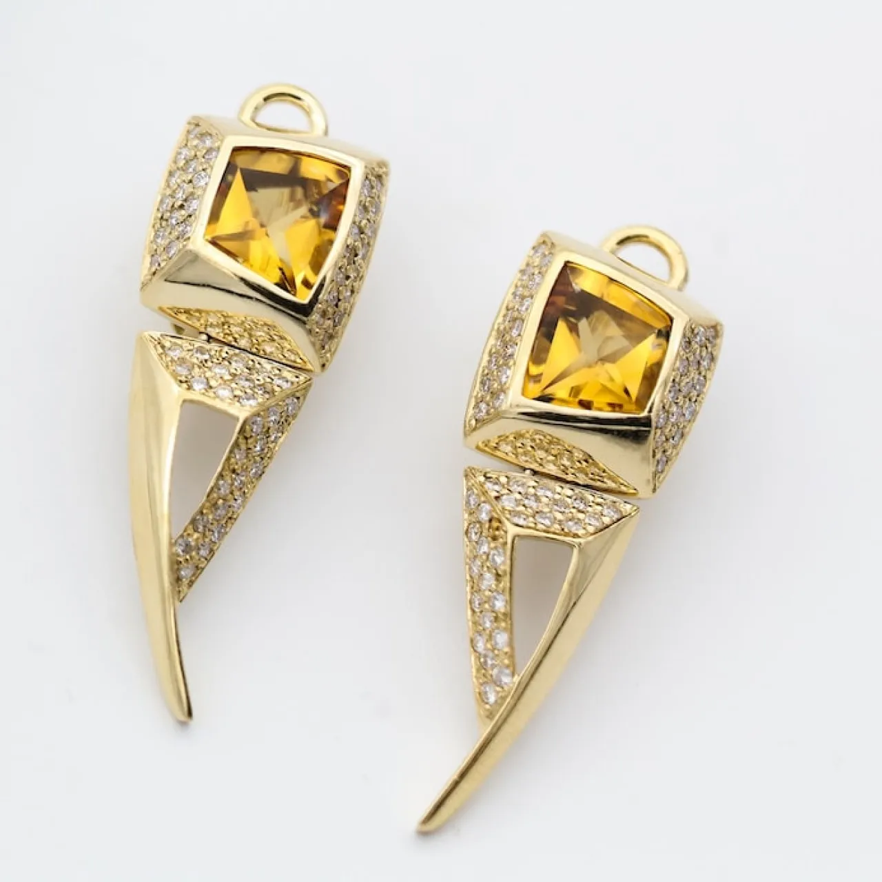 Pair of gold earrings with triangular yellow gemstones and small clear crystals on white background.